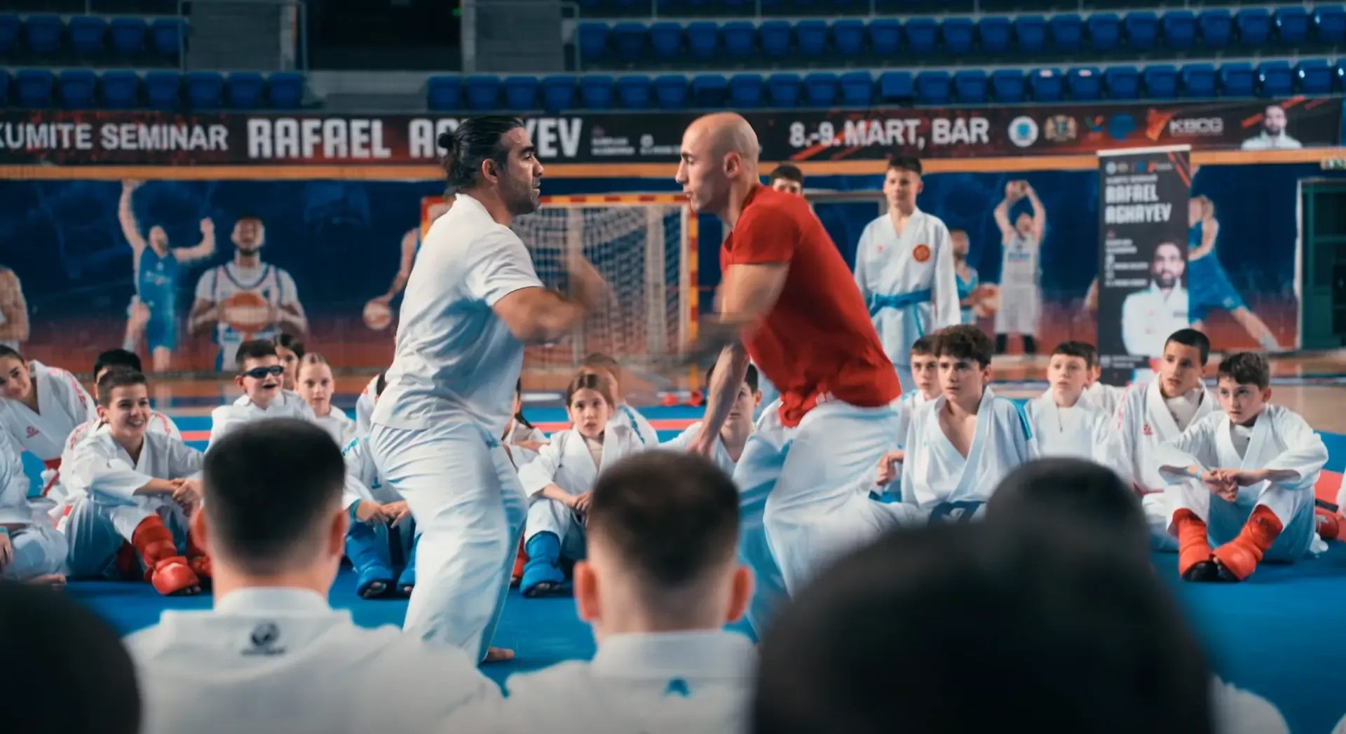 Karate seminar: dva instruktora demonstriraju tehniku pred djecom u kimonima.