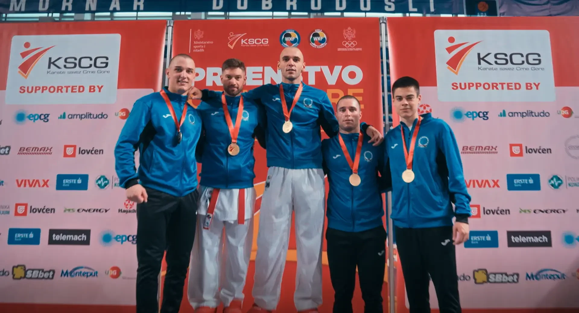 Članovi ekipe s medaljama zajedno poziraju pred takmičarskim panoom.