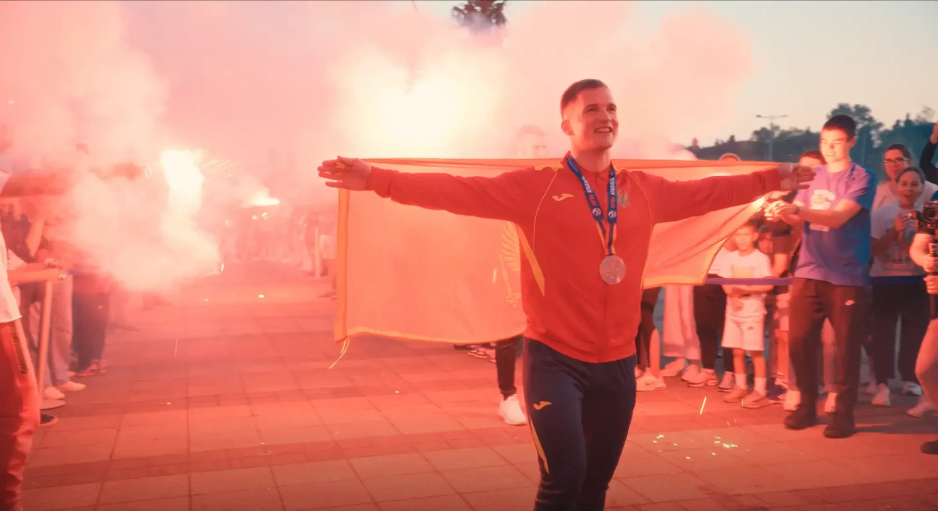 Sportista s medaljom širi crnogorsku zastavu pred okupljenima.