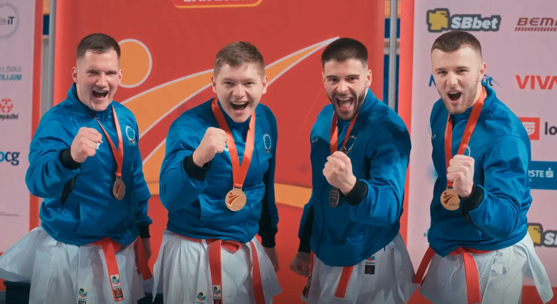 Četiri sportista u plavim trenercima s medaljama slave na pobjedničkom postolju.