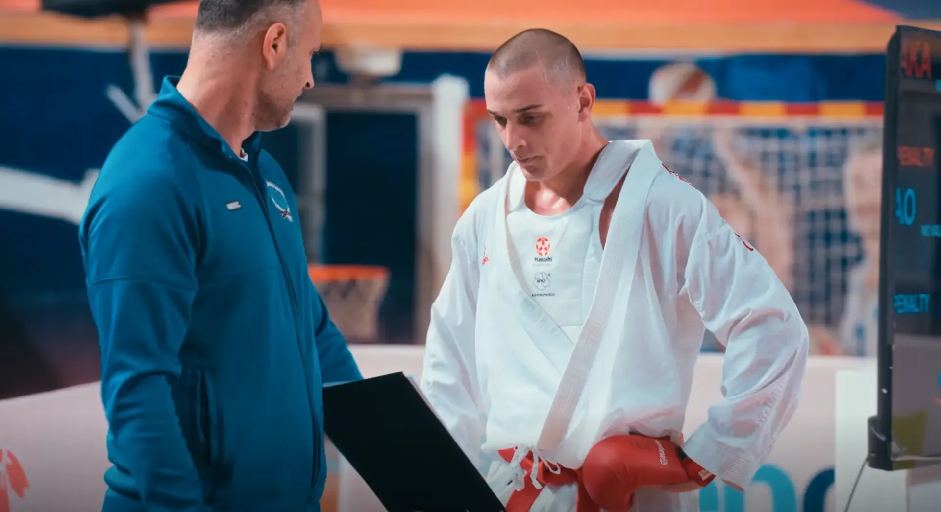 Trener razgovara sa sportistom pored tatamija.